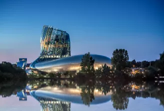 La Cité du Vin à Bordeaux, bâtiment architectural moderne avec façade inclinée illuminée, reflet dans l'eau calme au crépuscule
